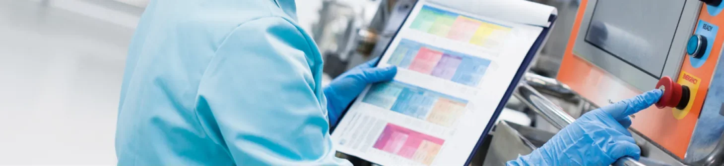 Operator in protective gloves checking a colour-coded production chart next to a machine control panel